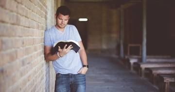 man leunt tegen bakstenen muur en leest boek