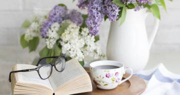 boek ligt open met bril erop op tafel met vaas paarse bloemen