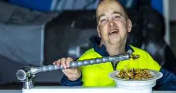 Een man houdt een verlengde lepen vast boven een bord met eten en kijkt lachend in de camera