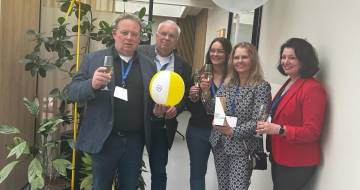 Twee mannen en drie vrouwen poseren lachend voor een tweetal ballonnen