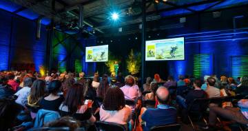 zaal vol mensen van de achterkant gefografeerd, kijkend naar een podium