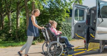 vrouw duwt rolstoel naar rolstoelbus