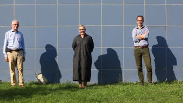 drie mensen staan voor een blauwe muur in de zon